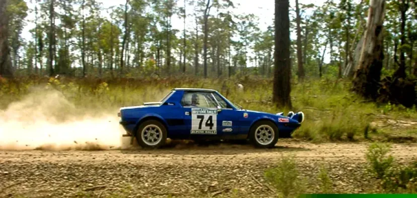 A blue rally car numbered 74 kicking up dust through Australian bushland on an alpine stage.