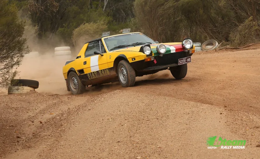 A yellow Fiat X1/9 rally car cresting a gravel rise at the Bagshot Rallysprint.